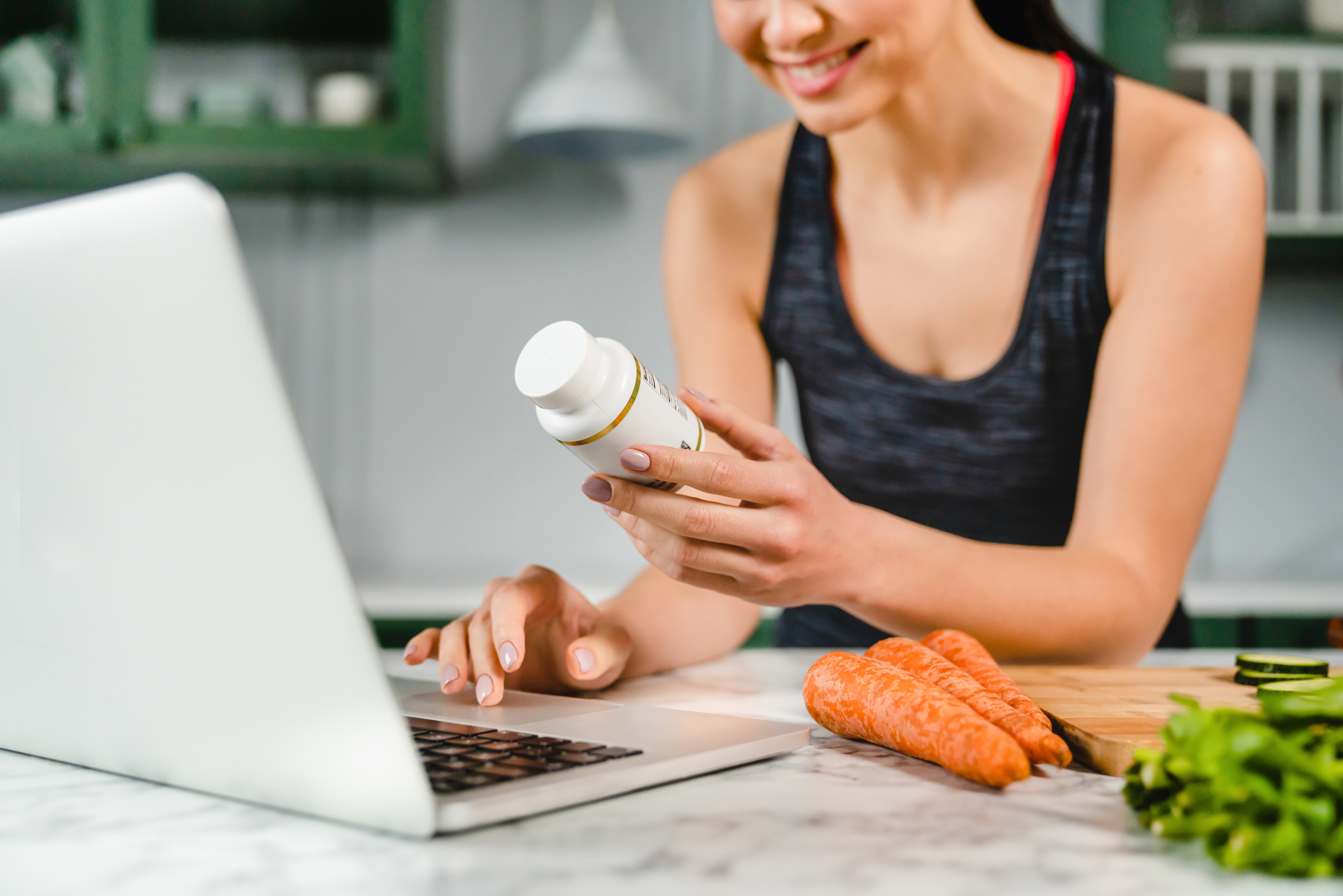 Happy young woman searching info in laptop about food supplements in the kitchen